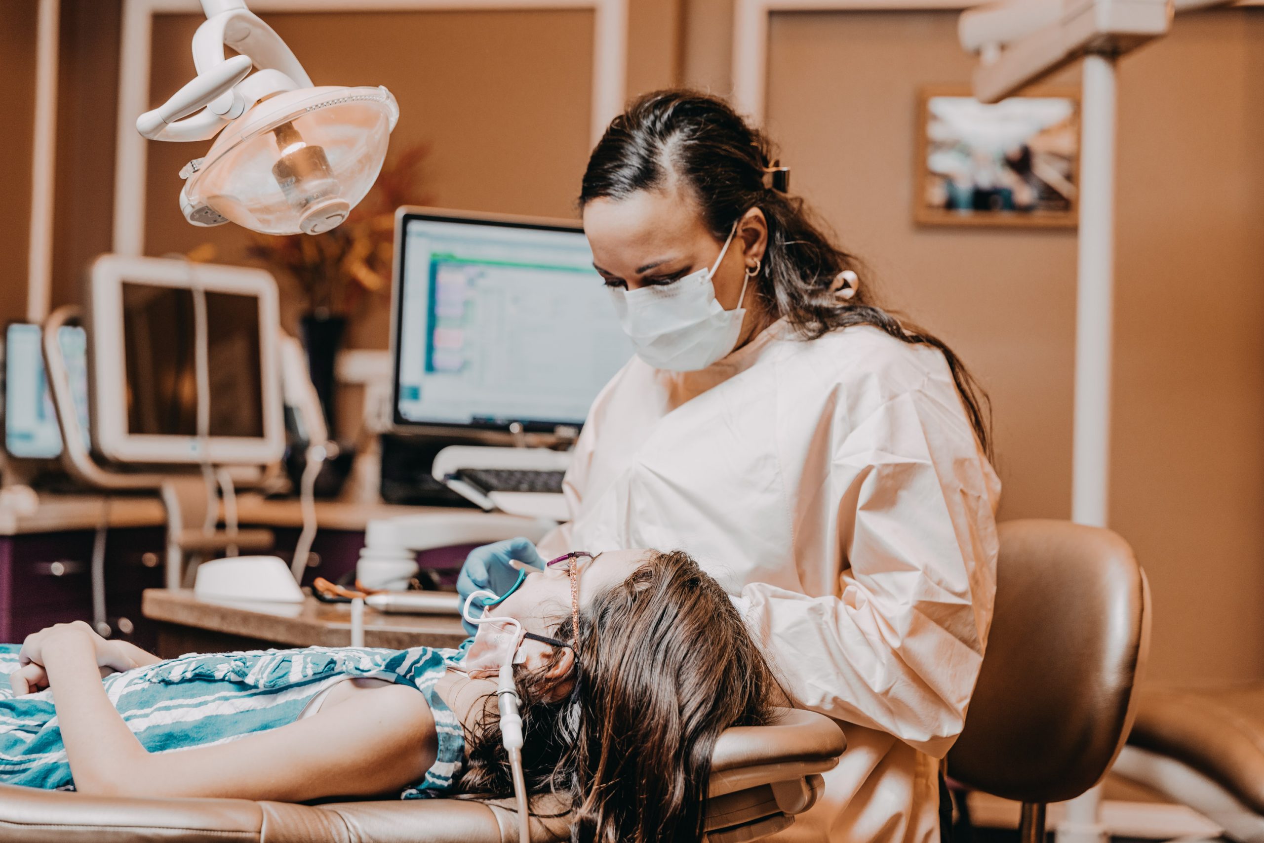 A dentist performs a dental procedure on a relaxed young girl in a comfortable chair. 