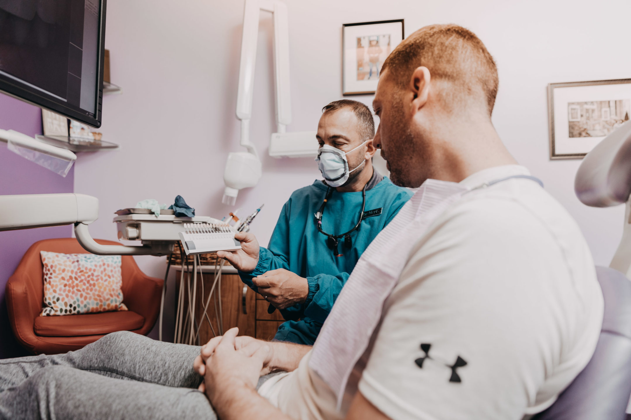 A dentist shows a patient a set of dental implants as he sits in the dental chair. 