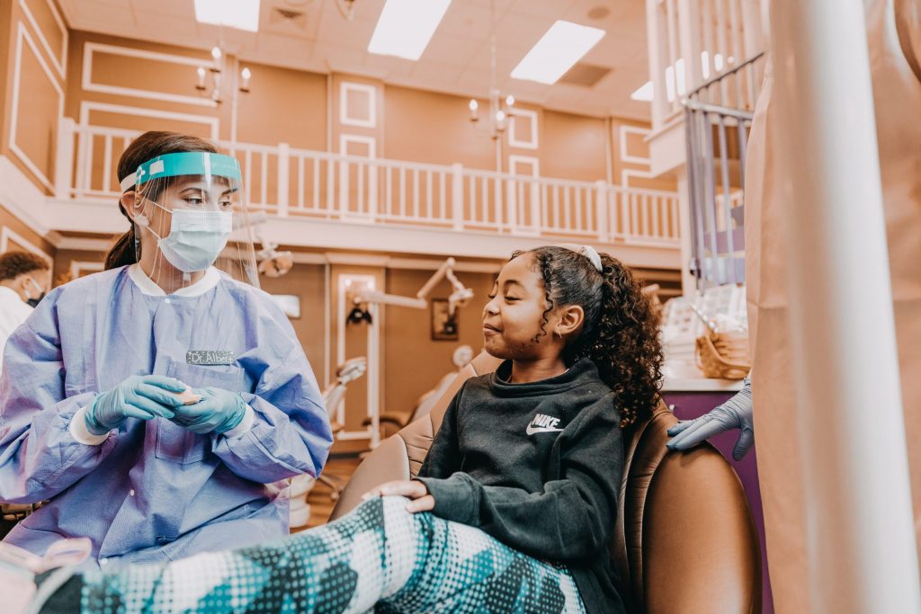  A pediatric dentist wearing personal protective equipment (PPE) provides dental care to a young girl. 