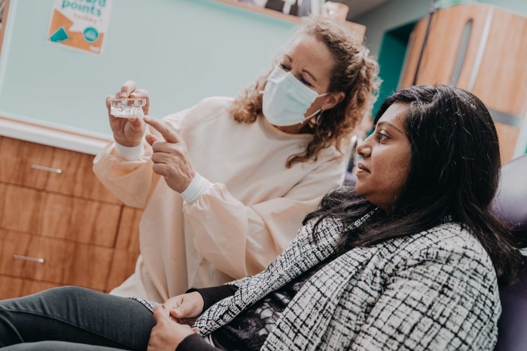 A dentist wearing a facemask shows a female adult patient how clear aligners work. 