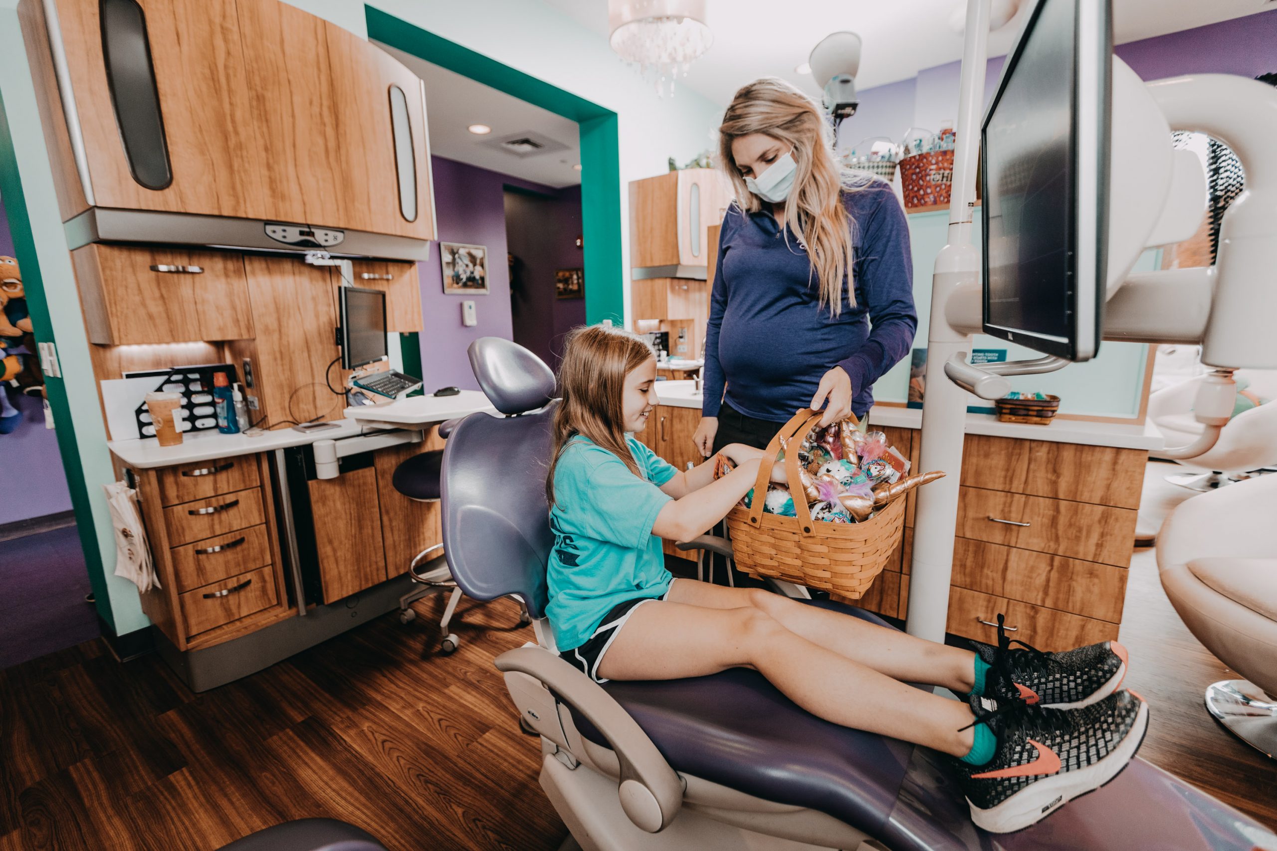 A young girl sitting in a Philadelphia dentist’s chair chooses a prize from an overflowing basket of gifts after her checkup.