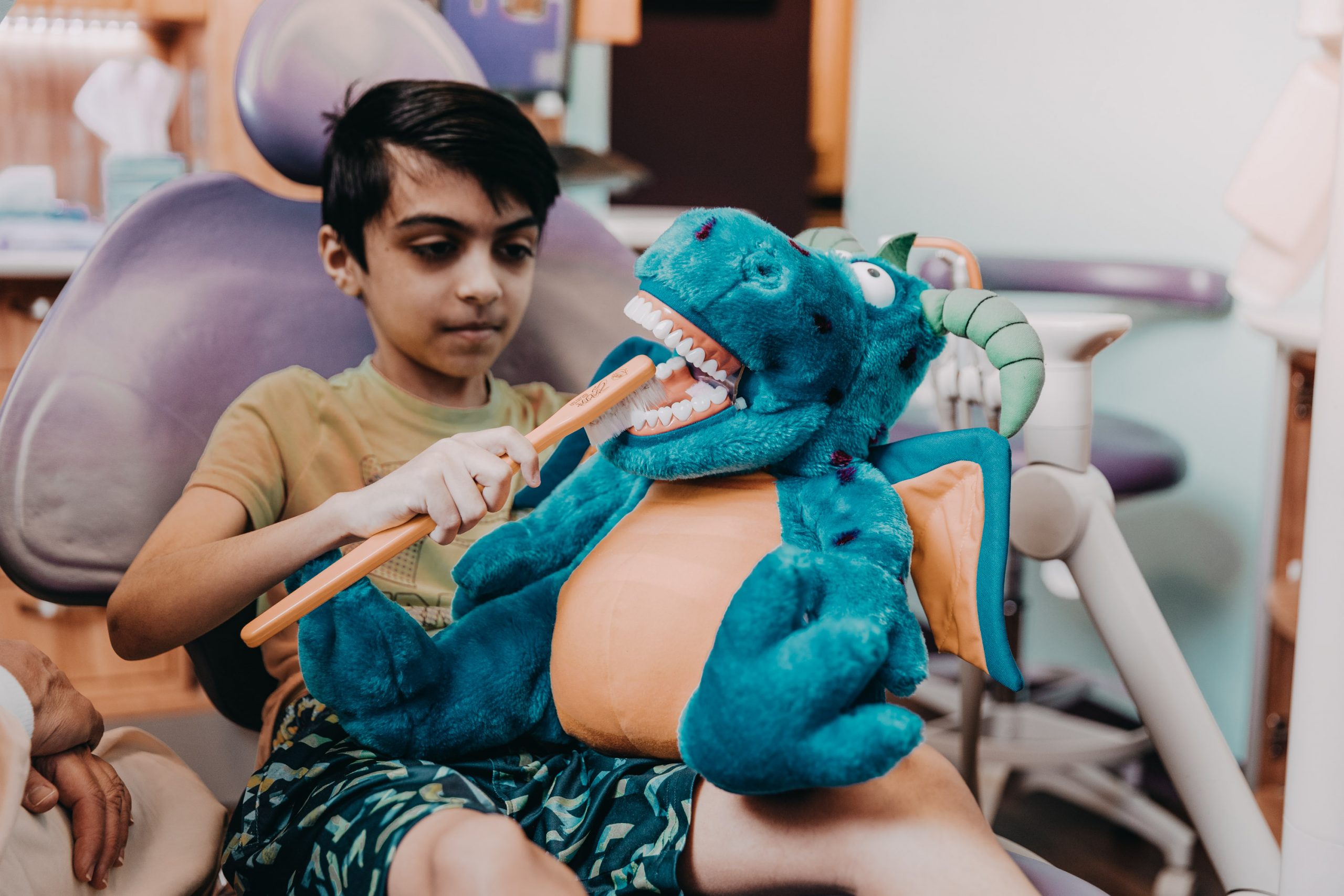 Young boy practices proper tooth brushing technique on a dinosaur puppet at the dental office. 