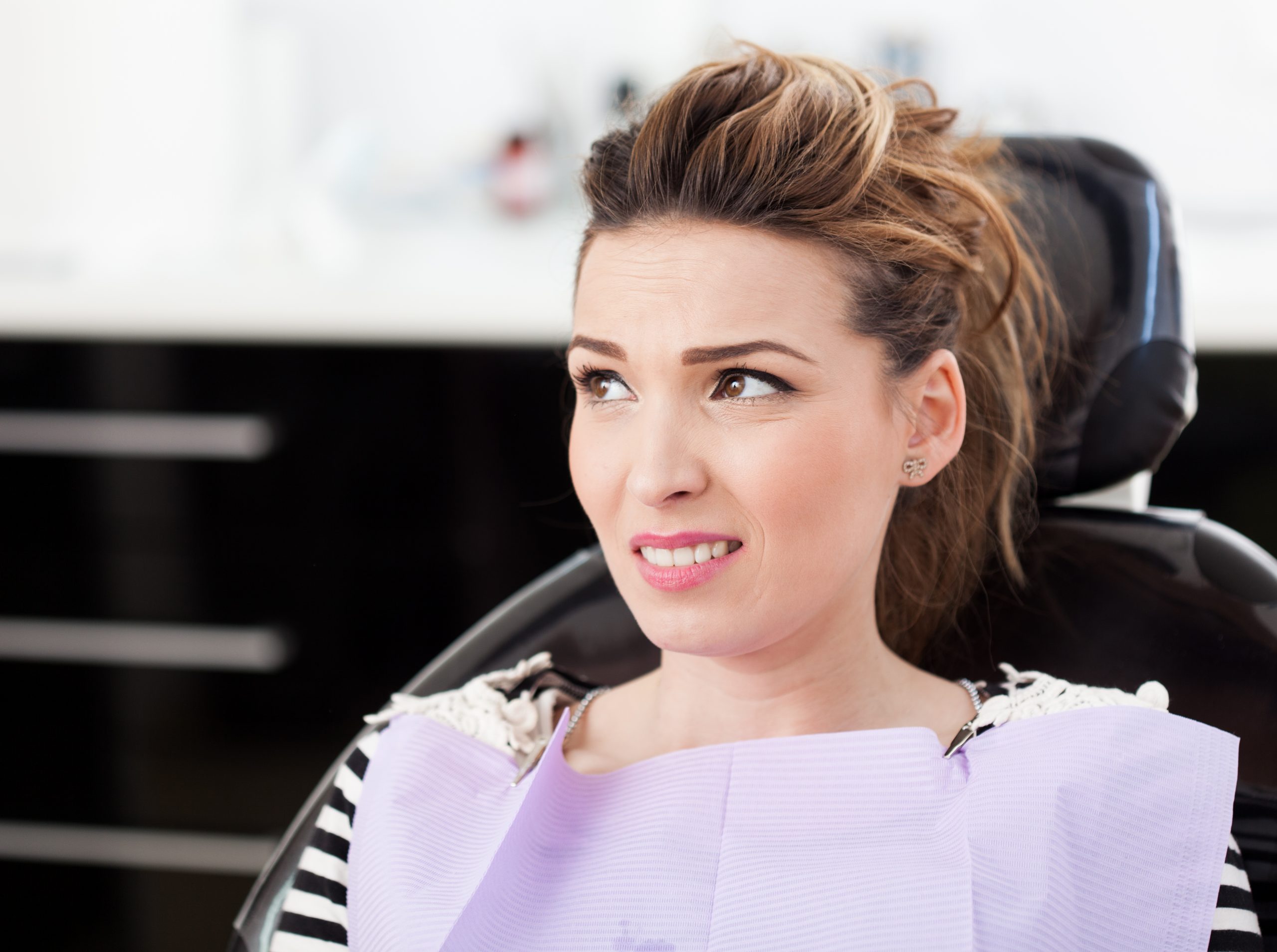 A female patient in a dentist chair looks concerned about dental treatment