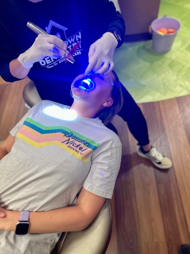 Image of an orthodontist treating a teenage patient wearing protective goggles and a gray T-shirt with colored stripes. 