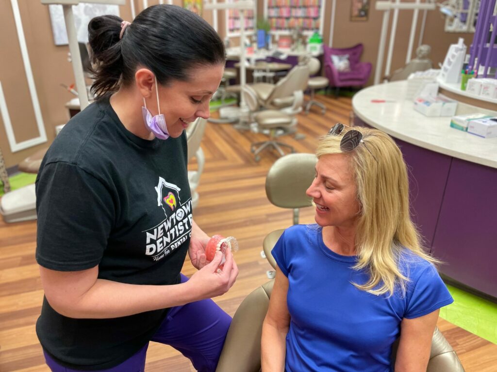 Image of a Newtown Dentistry orthodontist showing a female adult patient how Invisalign braces fit.