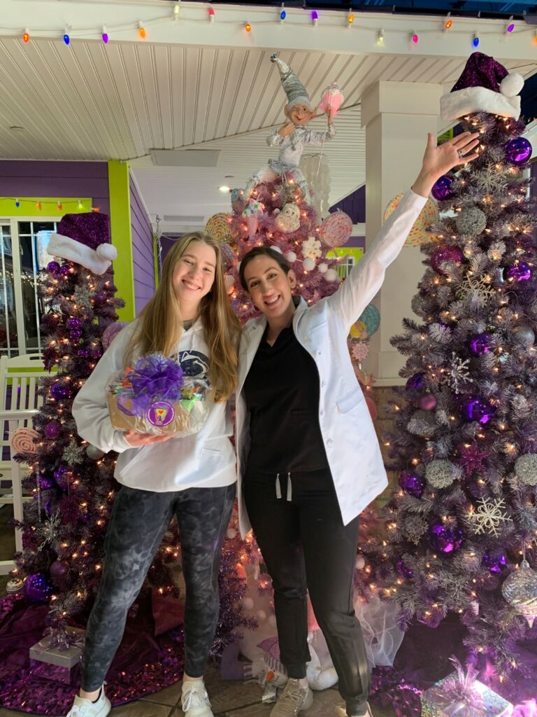 Image of teenage girl smiling with her orthodontist in front of decorated Christmas trees.