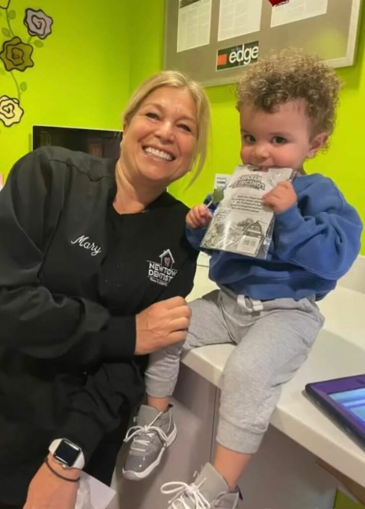 A baby sits in a dental office with a smiling dental assistant.