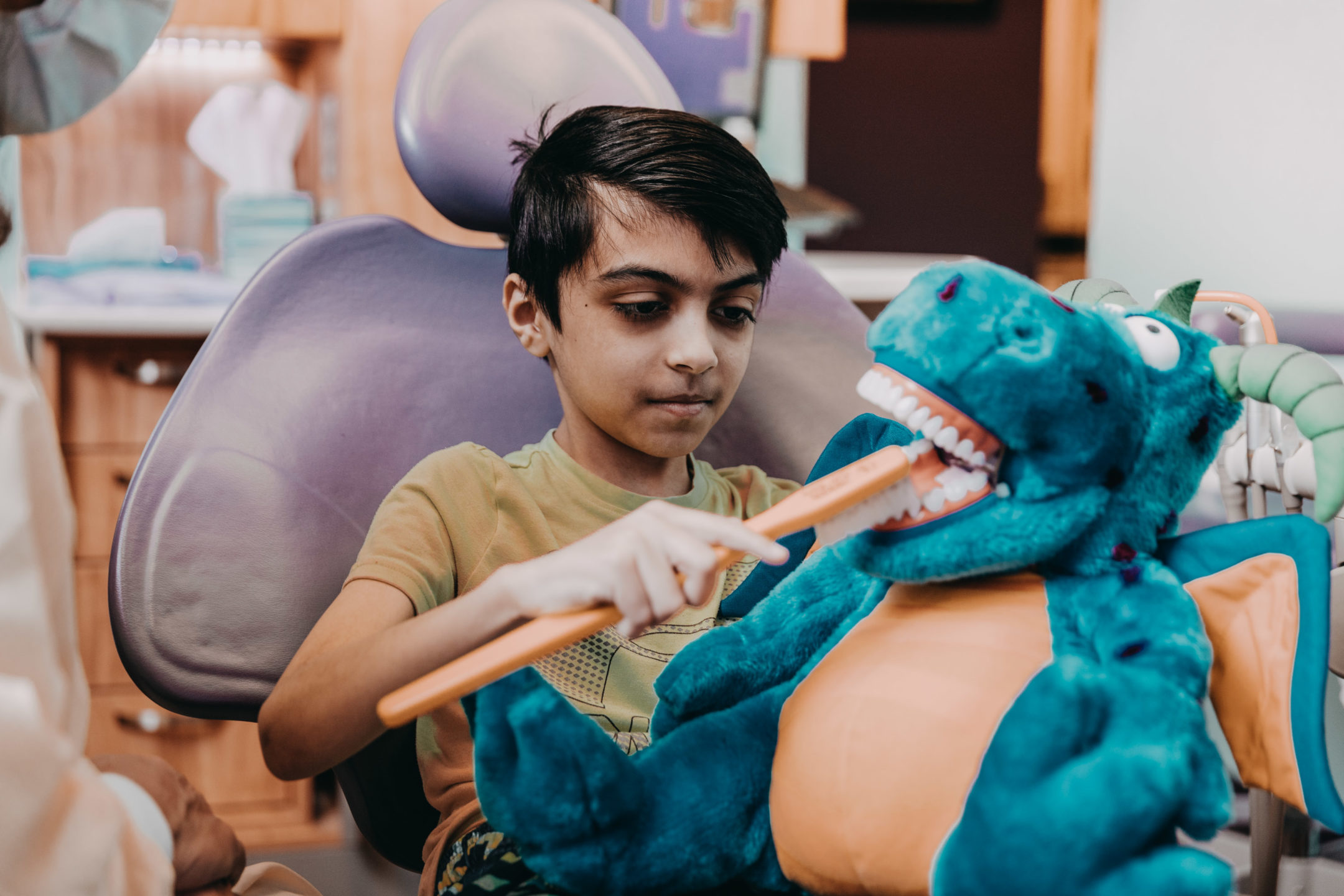 A young boy practices toothbrushing on a blue puppet.