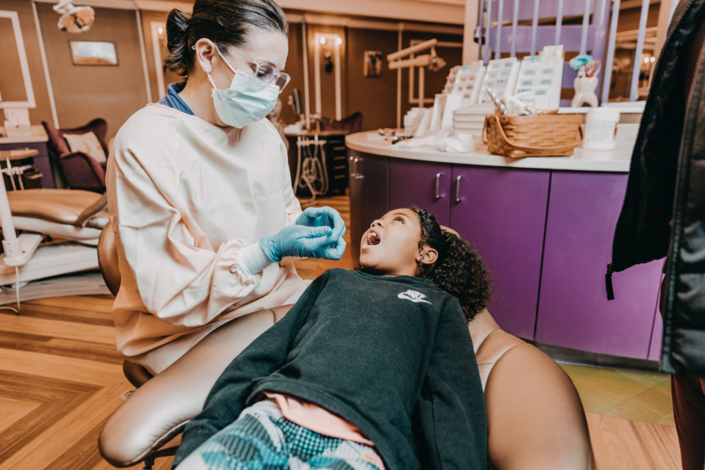  A girl lays back in a dental chair as a dentist examines her mouth. 
