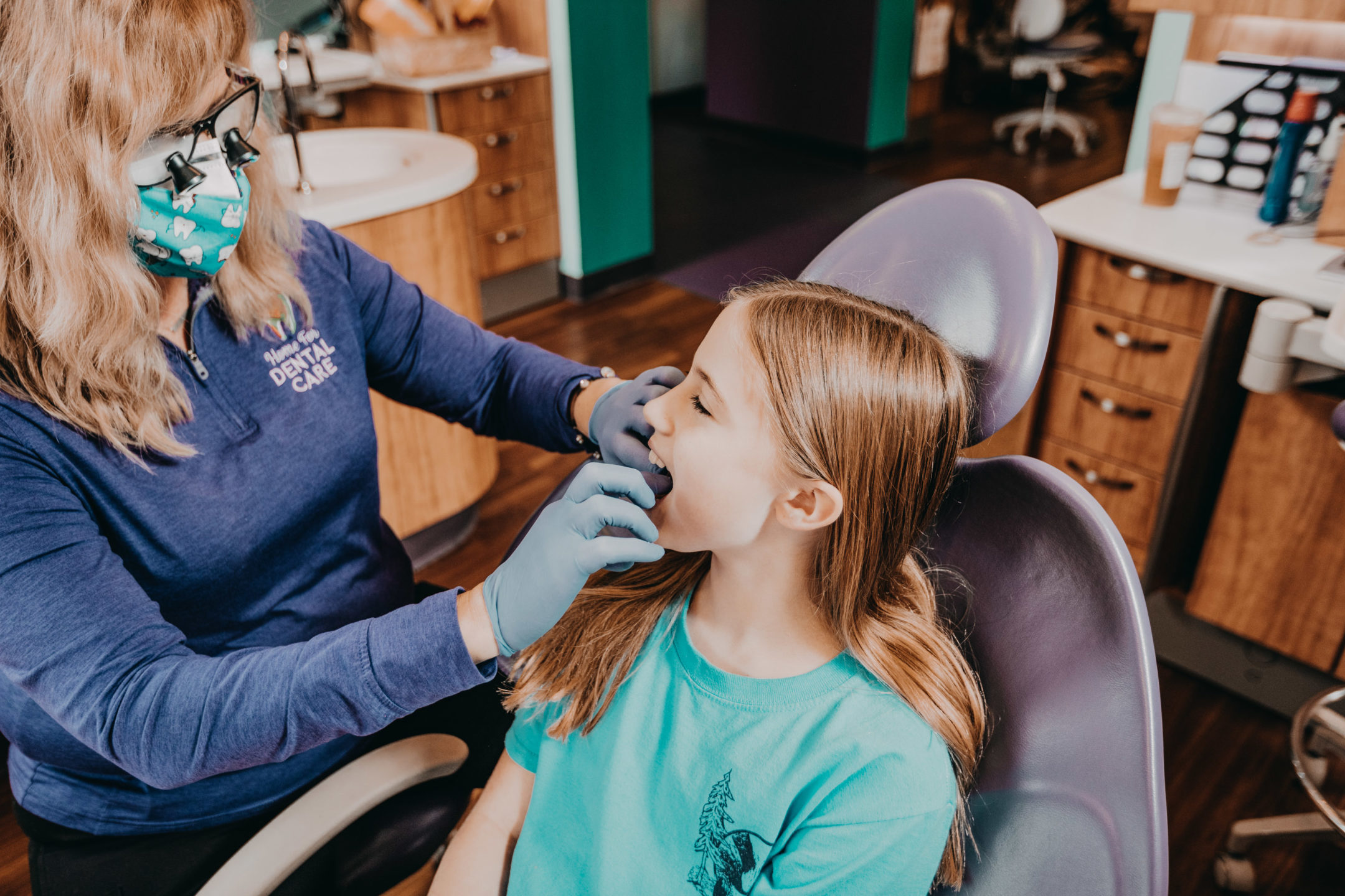 A child sits in a dental chair as a dentist examines her mouth. 