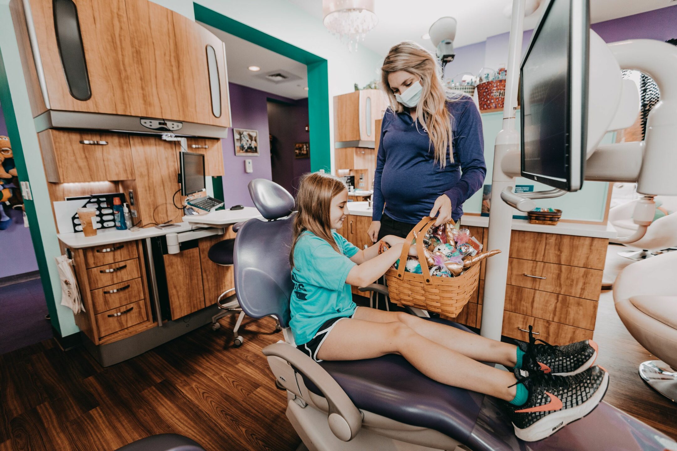  A child in a dental chair picks a toy from a basket. 