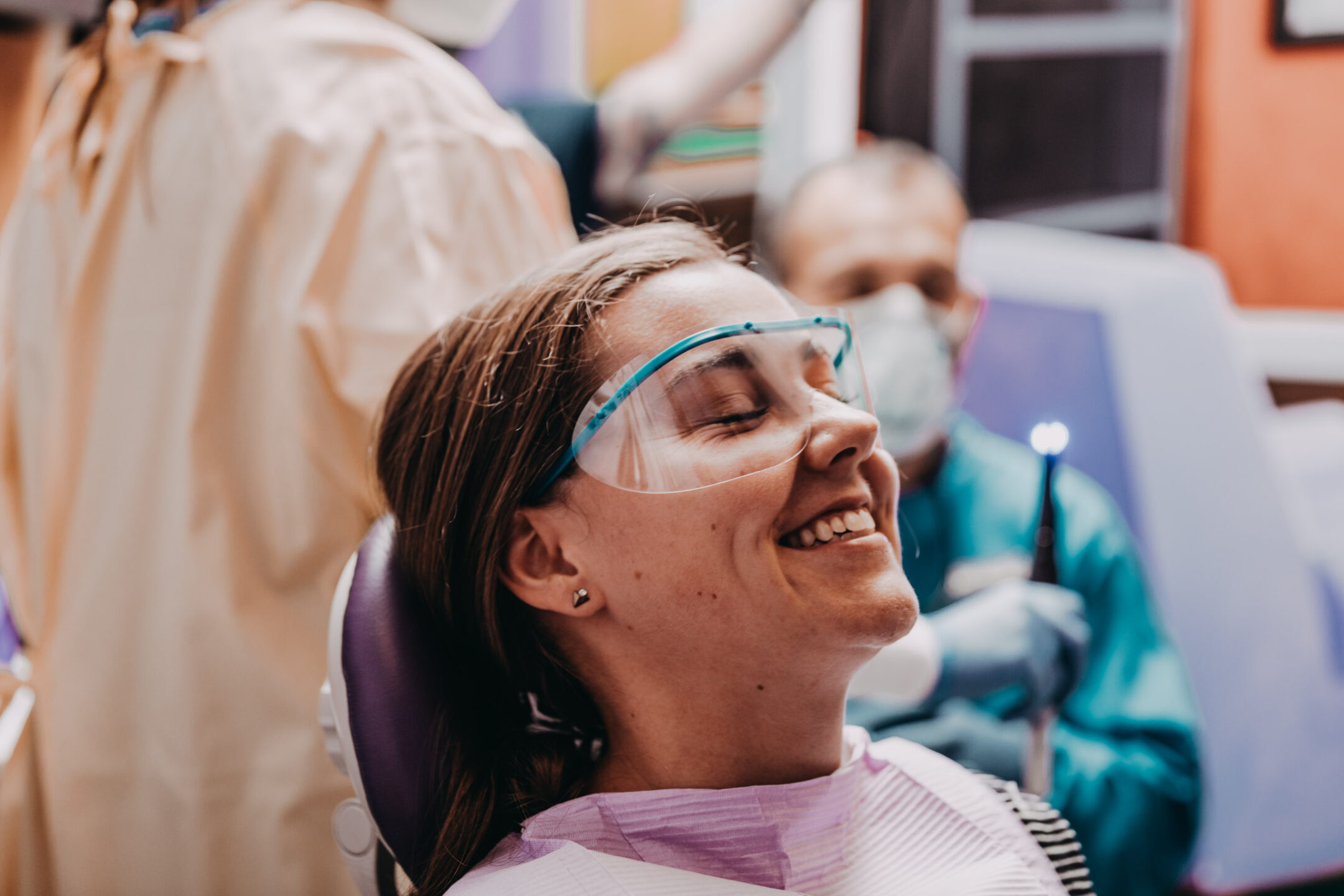  Female dental patient smiling in dentist’s chair and wearing protective goggles.