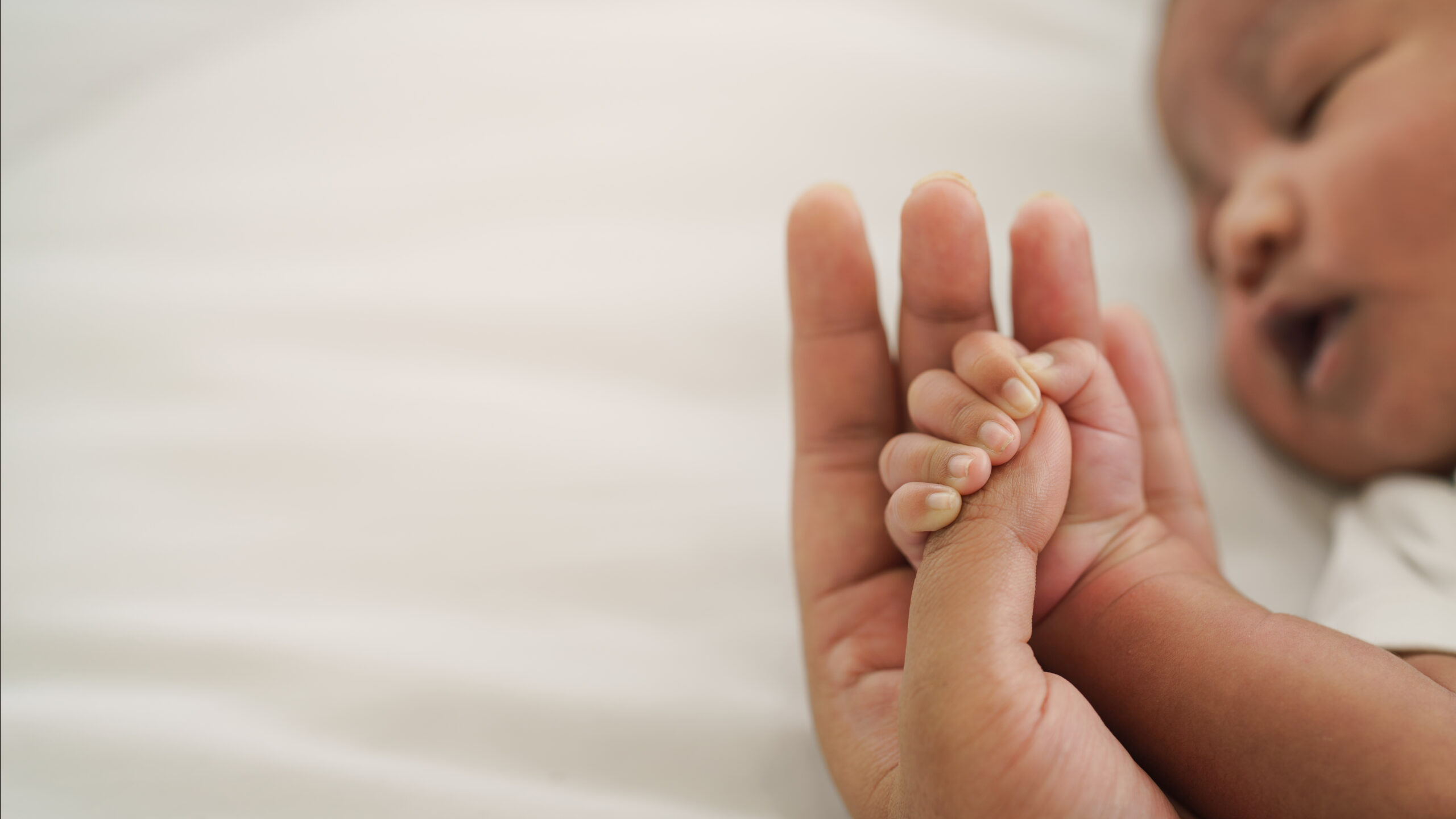 Image of infant lying down holding adult’s hand.