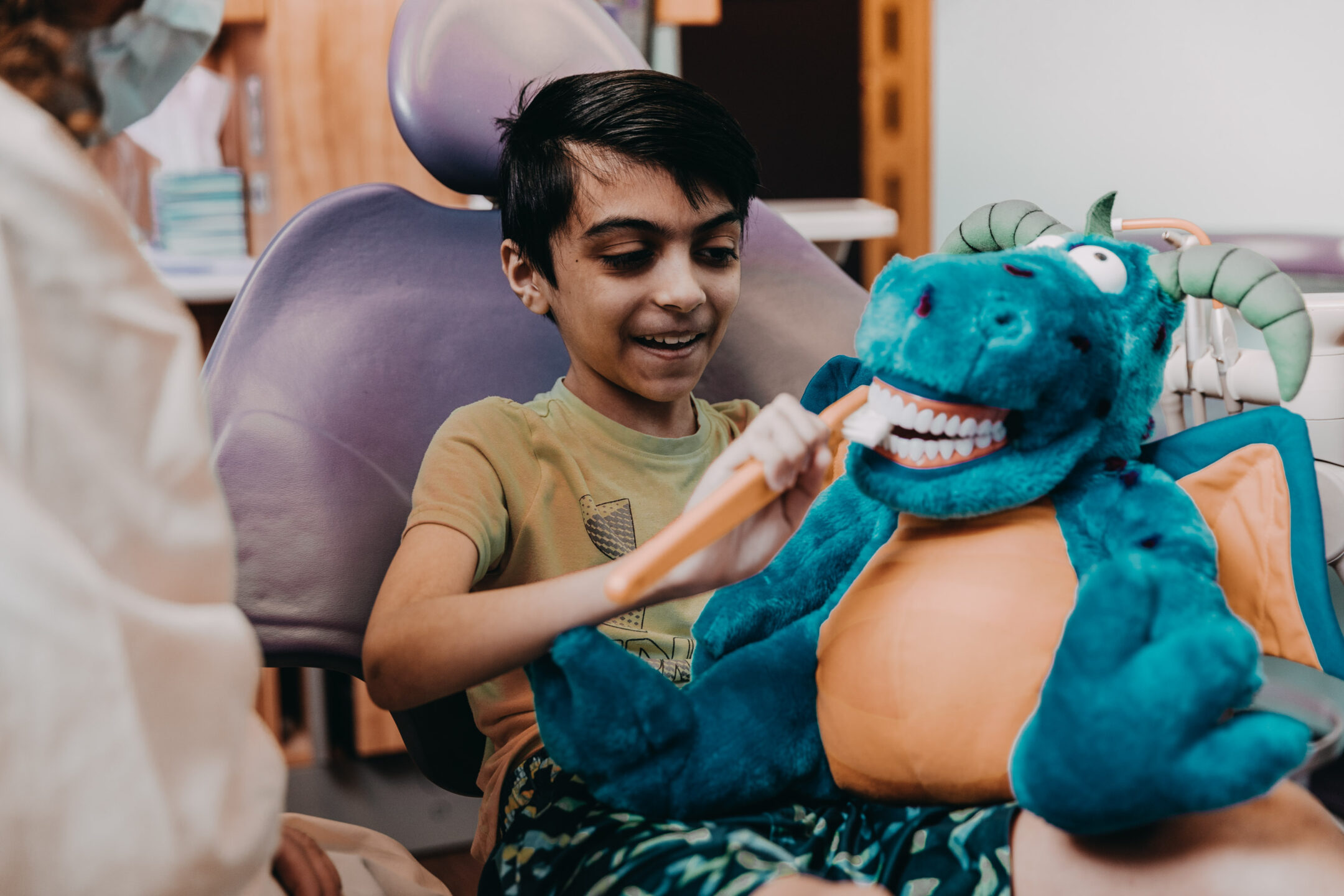 Image of young boy learning how to brush teeth properly on a blue animal puppet. 