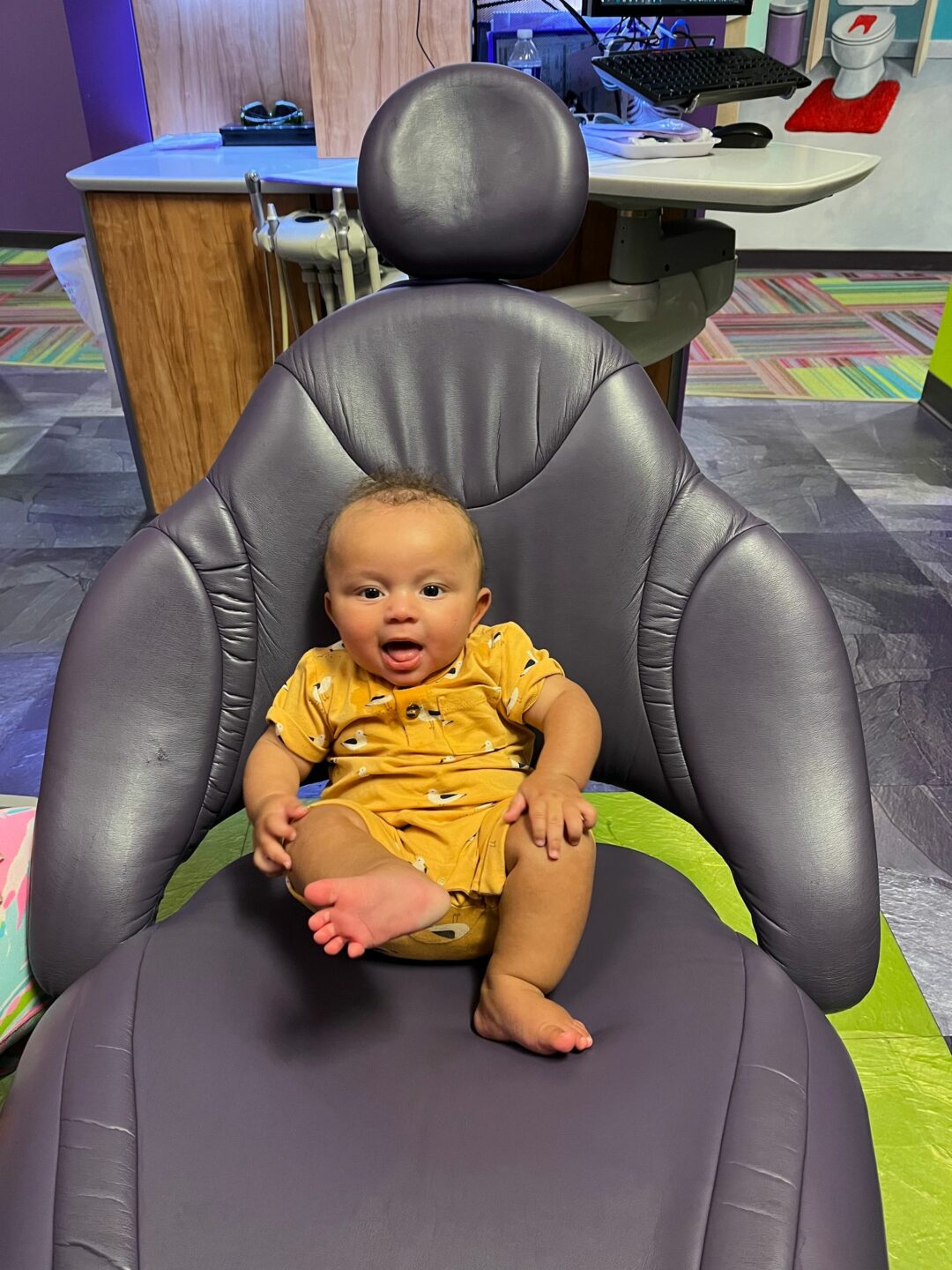 Image of happy infant sitting in dental chair at the dentist’s office.