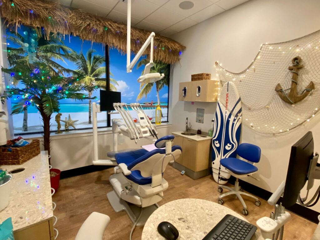 Image of adult dental treatment room with an underwater theme, with blue chair, surfboard, anchor, and dental equipment. 