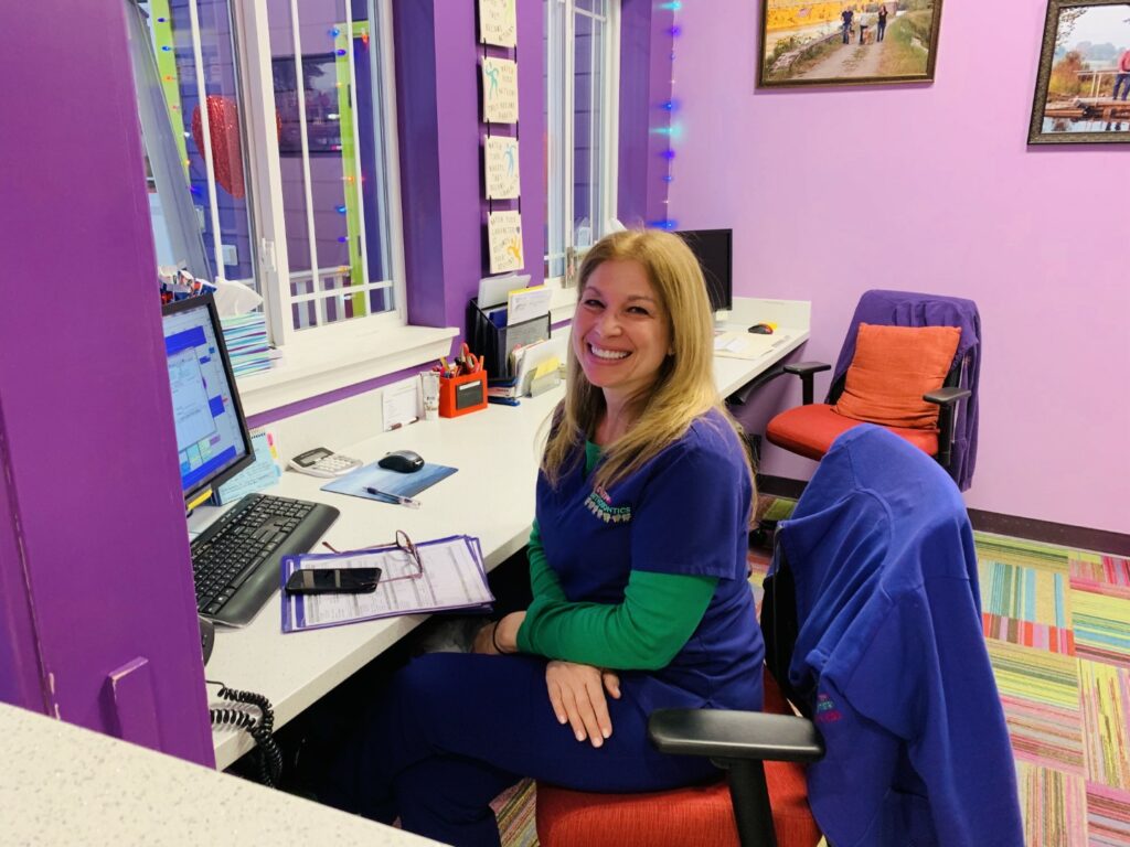 A smiling receptionist sits at the reception desk in a colorful dental office.