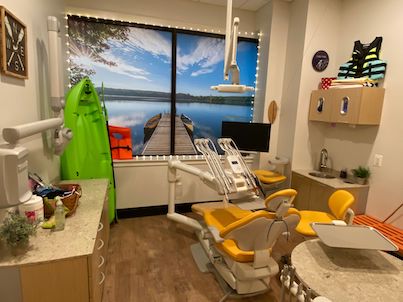 Image of adult dental treatment room with lakeside boating theme, with yellow dental chair, green kayak, and dentist tools.