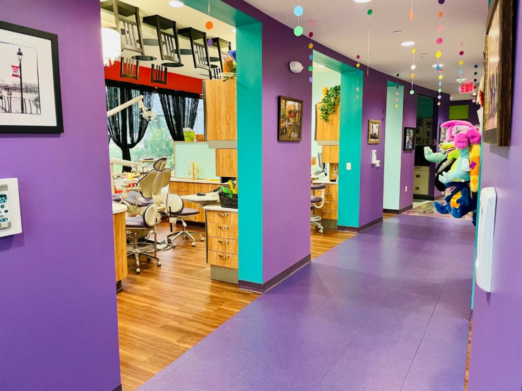 Image of a brightly colored pediatric dentist office with purple walls and floor, stuffed animals, and streamers. 