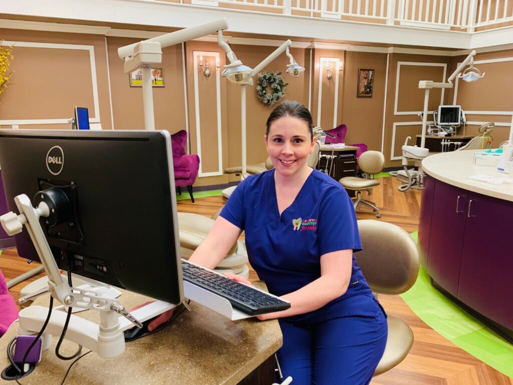 Orthodontist assistant smiling and wearing scrubs while posing at desk